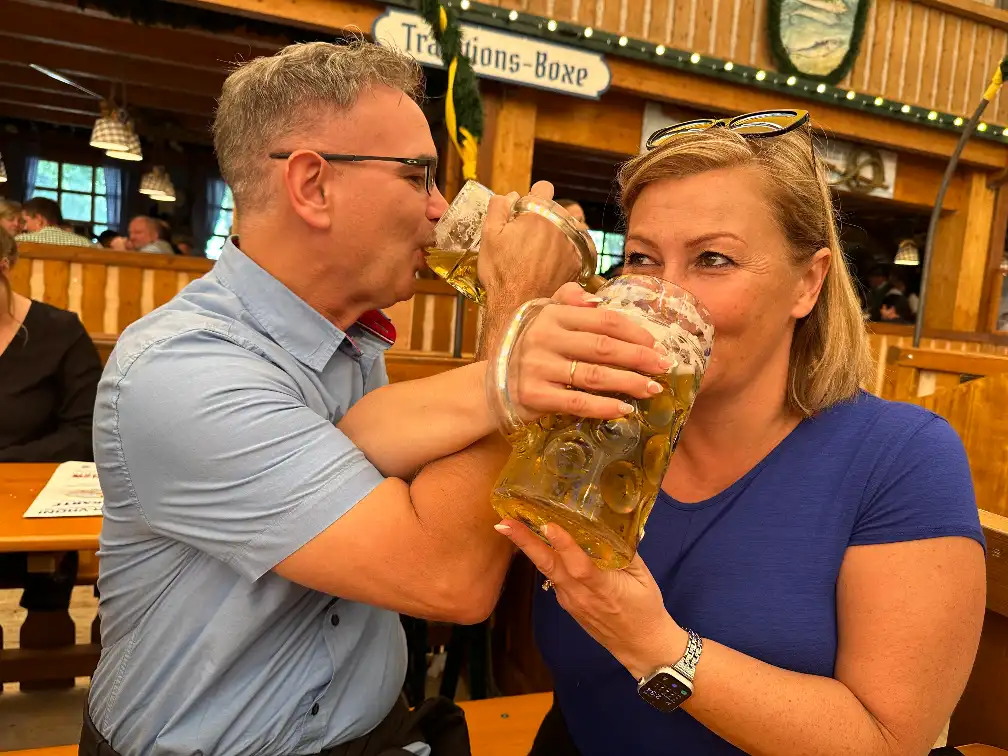 Friends linking arms and toasting with one-litre beer steins at Oktoberfest