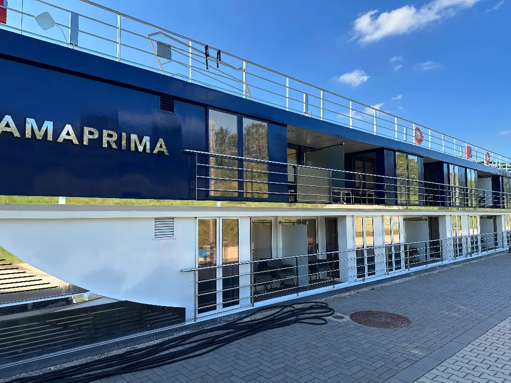 A long, low river cruise boat tied up to a European riverside pier